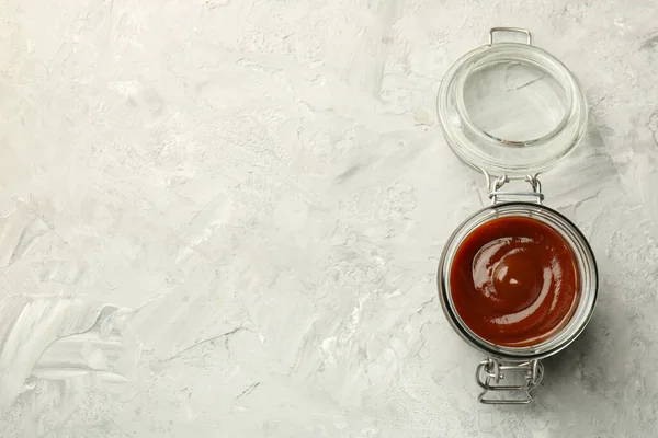 Tasty barbeque sauce in open jar on grey textured table, top view. Space for text