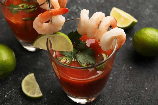 Tasty shrimp cocktail with sauce in glasses and limes on grey textured table, closeup