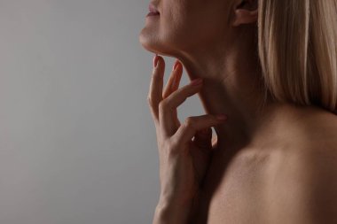 Gri arka planda boynuna dokunan kadın, yakın plan. Metin için boşluk