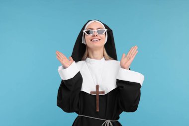 Mavi arka planda güneş gözlüklü, rahibe kıyafetli mutlu kadın.