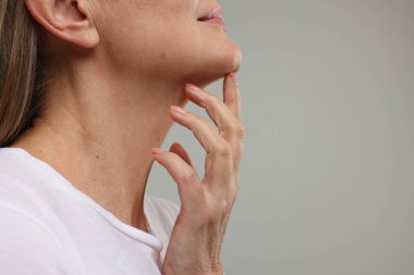 Gri arka planda sağlıklı cilde sahip olgun bir kadın, yakın plan. Metin için boşluk