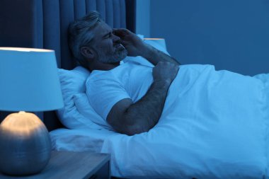 Yetişkin bir adam gece yatağında baş ağrısı çekiyor.