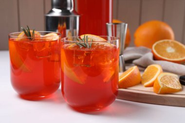 Aperol spritz kokteyli, biberiye ve portakal dilimleri beyaz ahşap masada.