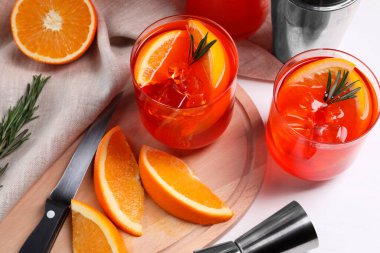 Aperol spritz kokteyli, biberiye ve portakal dilimleri beyaz ahşap masada, üst tarafta.