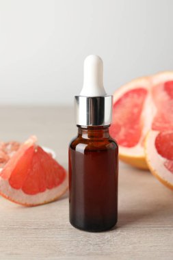 Şişede greyfurt yağı ve açık ahşap masada meyve, yakın plan.
