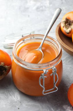 Lezzetli hurma reçeli ve gri masada taze meyveler.