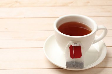Hafif ahşap masada çay poşeti ve bir fincan sıcak içecek, yakın plan. Metin için boşluk