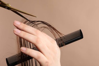 Kuaför açık kahverengi arka planda makasla müşterinin saçını kesiyor.