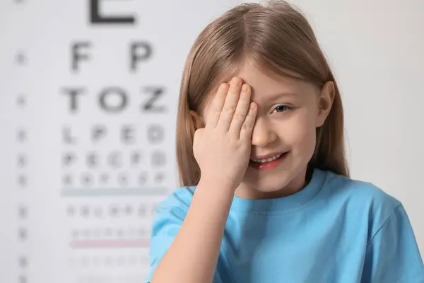 Little girl covering her eye against vision test chart