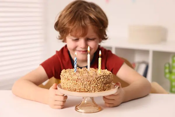 Cute boy with birthday cake at table indoors