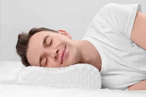 Man sleeping on orthopedic pillow against light grey background
