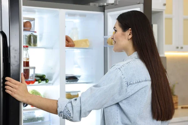 Young woman near modern refrigerator in kitchen