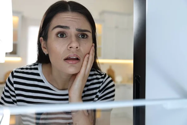 Upset woman near empty refrigerator in kitchen, view from inside
