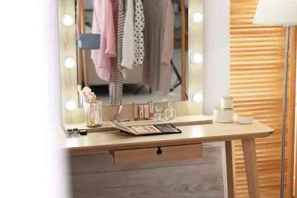 Makeup room. Stylish mirror with light bulbs and different beauty products on dressing table indoors