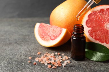 Pipetten şişeye greyfurt yağı damlatıyor, deniz tuzu ve taze meyveler karanlık masaya dökülüyor, yakın plan. Metin için boşluk