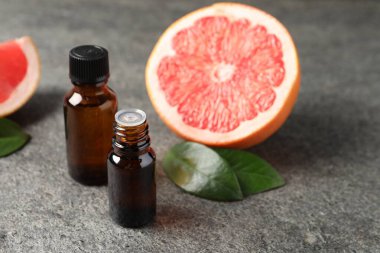 Şişelerde greyfurt yağı, yapraklar ve meyveler koyu dokulu masa üzerinde, yakın çekim