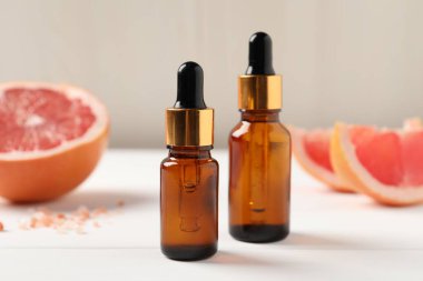 Beyaz ahşap masadaki şişelerde greyfurt yağı, yakın plan.