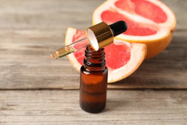 Şişede greyfurt yağı, pipet ve meyveler ahşap masada, yakın plan.