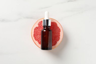 Şişede greyfurt yağı ve beyaz mermer masa üzerinde yarım meyve.