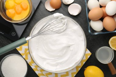 Krem şantili kase, çırpılmış çırpılmış ve malzemeler siyah masada, düz yerde.