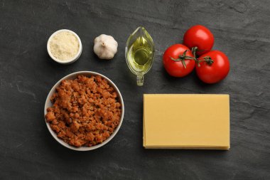 Koyu dokulu masada lazanya pişirmek için kullanılan ürünlerle düz bir kompozisyon.