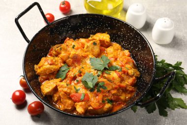 Tavada körili tavuk, maydanoz ve domatesler açık gri masada, yakın plan.