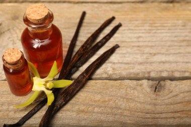 Aromatik vanilya özü, kapsüller ve çiçek ahşap masada, yakın plan. Metin için boşluk