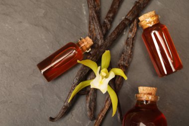 Aromatik vanilya özü, kapsüller ve çiçekler siyah masada, düz yatıyordu.