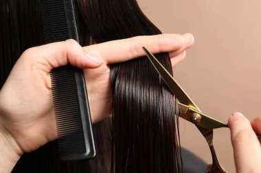 Kuaför açık kahverengi arka planda makasla müşterinin saçını kesiyor.