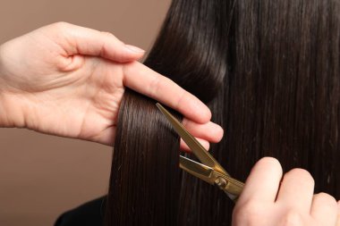 Kuaför açık kahverengi arka planda makasla müşterinin saçını kesiyor.