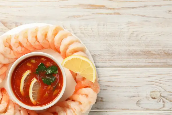Tasty boiled shrimps with cocktail sauce and lemon on white wooden table, top view. Space for text