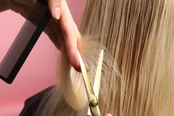 Hairdresser cutting client\'s hair with scissors on pink background, closeup