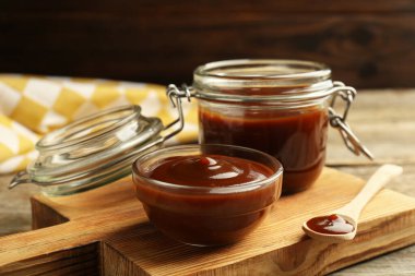 Lezzetli barbekü sosu kasede, kavanoz ve kaşık ahşap masada, yakın plan.