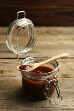 Kavanozda lezzetli barbekü sosu ve tahta masada kaşık.