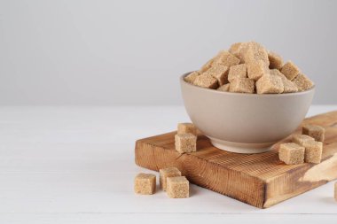 Brown sugar cubes on white wooden table, space for text