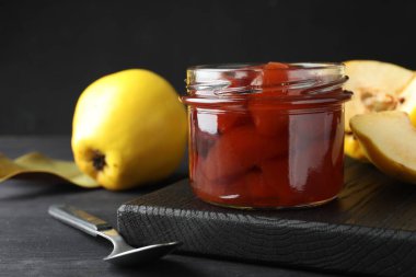 Ayva reçeli cam kavanozda, kaşık ve taze çiğ meyveler gri masada, yakın plan.