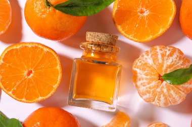 Aromatik mandalina yağı şişede, yapraklar ve narenciye meyveleri beyaz masada, düzdü.