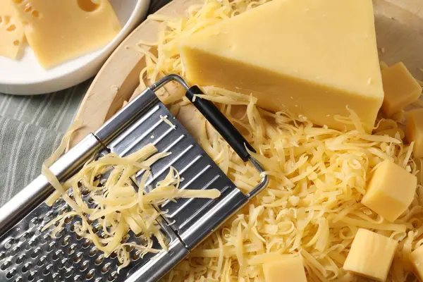 Grated, whole pieces of cheese and grater on table, top view