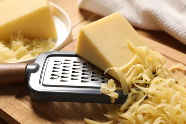 Grated, whole piece of cheese and grater on table, closeup