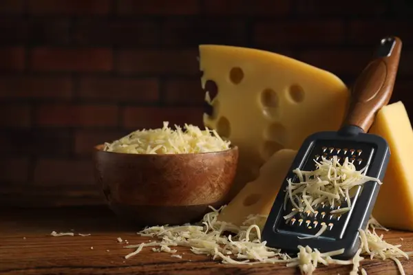 Grated, cut cheese and grater on wooden board, closeup