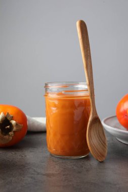 Cam kavanozdaki lezzetli hurma reçeli gri masada servis edilir.