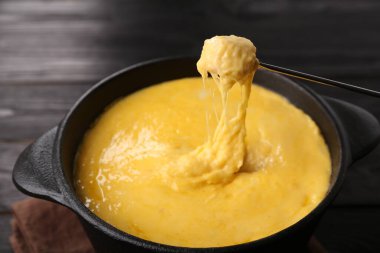 Jambonu fondü kabına daldırmak, erimiş peyniri siyah ahşap masaya koymak, yakın plan.