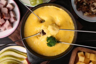 Farklı ürünleri fondü kabına batırıp erimiş peyniri siyah ahşap masaya koyup, düz bir şekilde yatırmak.