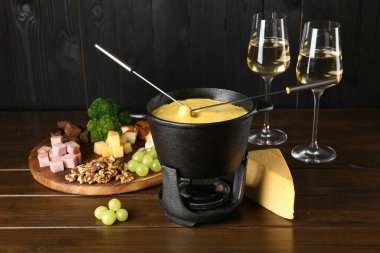 Erimiş peynirli fondü tenceresi, bir bardak şarap ve ahşap masada farklı ürünler.