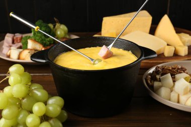 Eritilmiş peynirli fondü kabı, çatallar ve ahşap masada farklı ürünler, yakın plan.