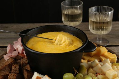 Erimiş peynirli fondü kabı, bir bardak şarap ve ahşap masada farklı ürünler, yakın plan.