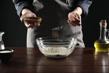 Ekmek yapıyorum. Ahşap masada kuru mayayı kaseye koyan kadın, yakın plan.