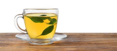 Beyaz arka planda, tahta masada fincanda yeşil çay tazeleniyor.