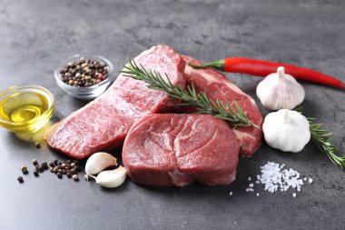 Gri masada çiğ biftek, yağ ve baharatlar.