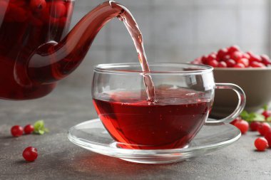 Sıcak yaban mersini çayını cam fincana ve taze böğürtlenleri açık gri desenli masaya döküyorum. Yakın plan.